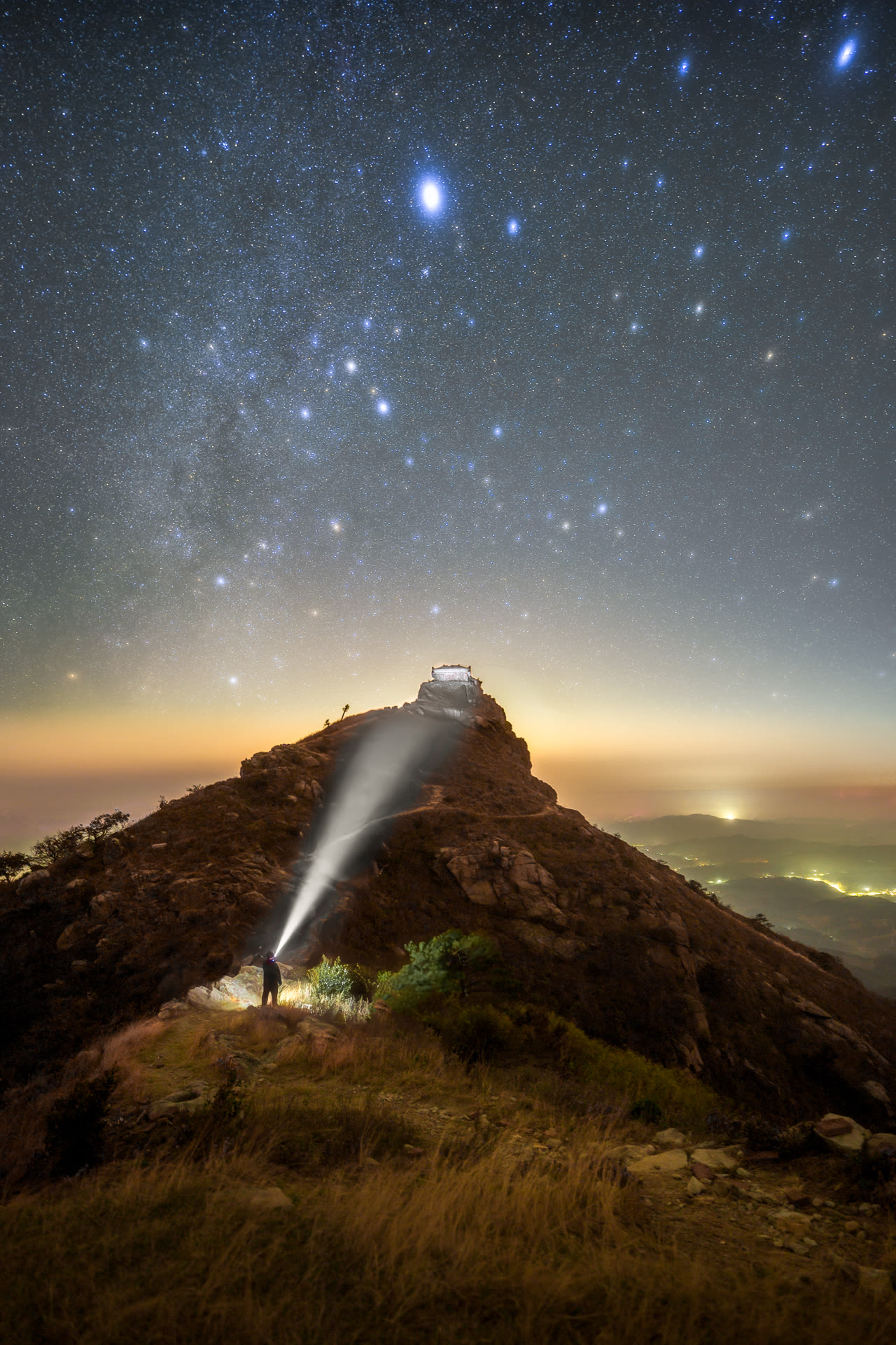 星空下站在山顶拍摄的摄影师背影